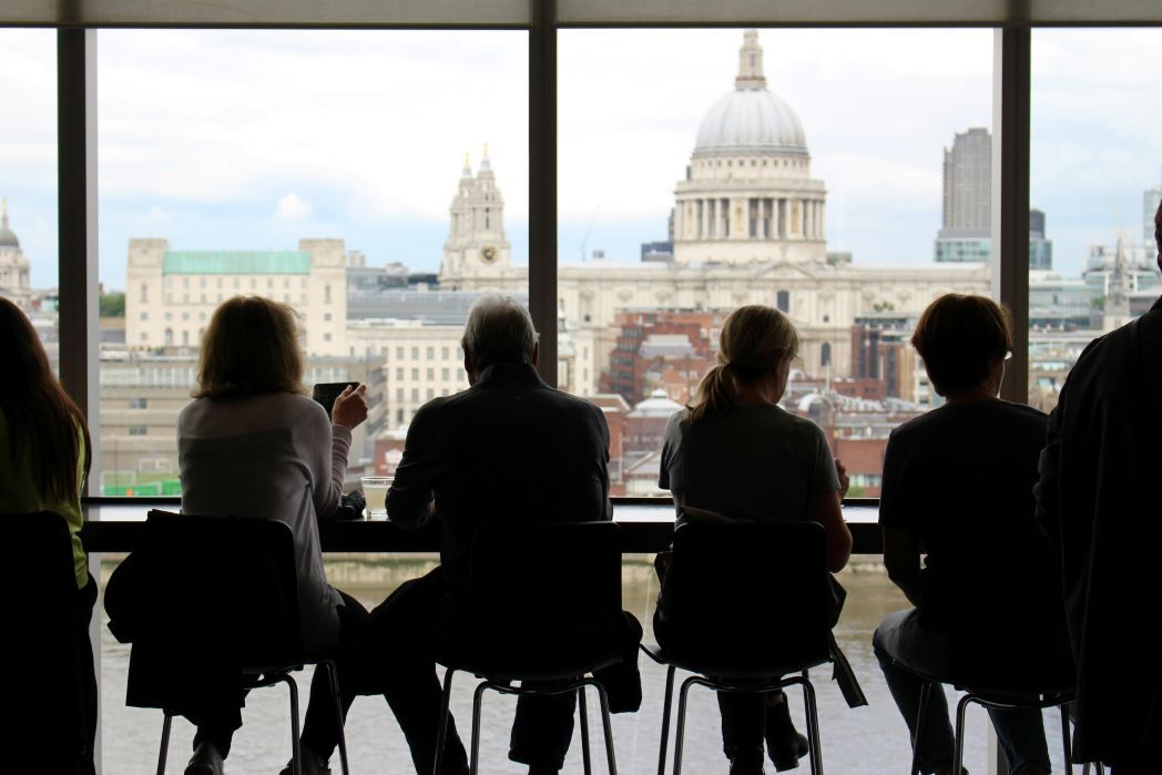 A group of people sit in silhouette against a window overlooking London