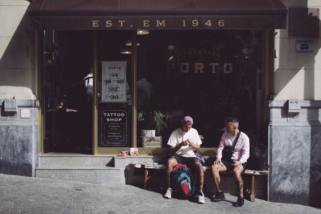 Two men sit outside a tattoo parlour forming a connection as they wait