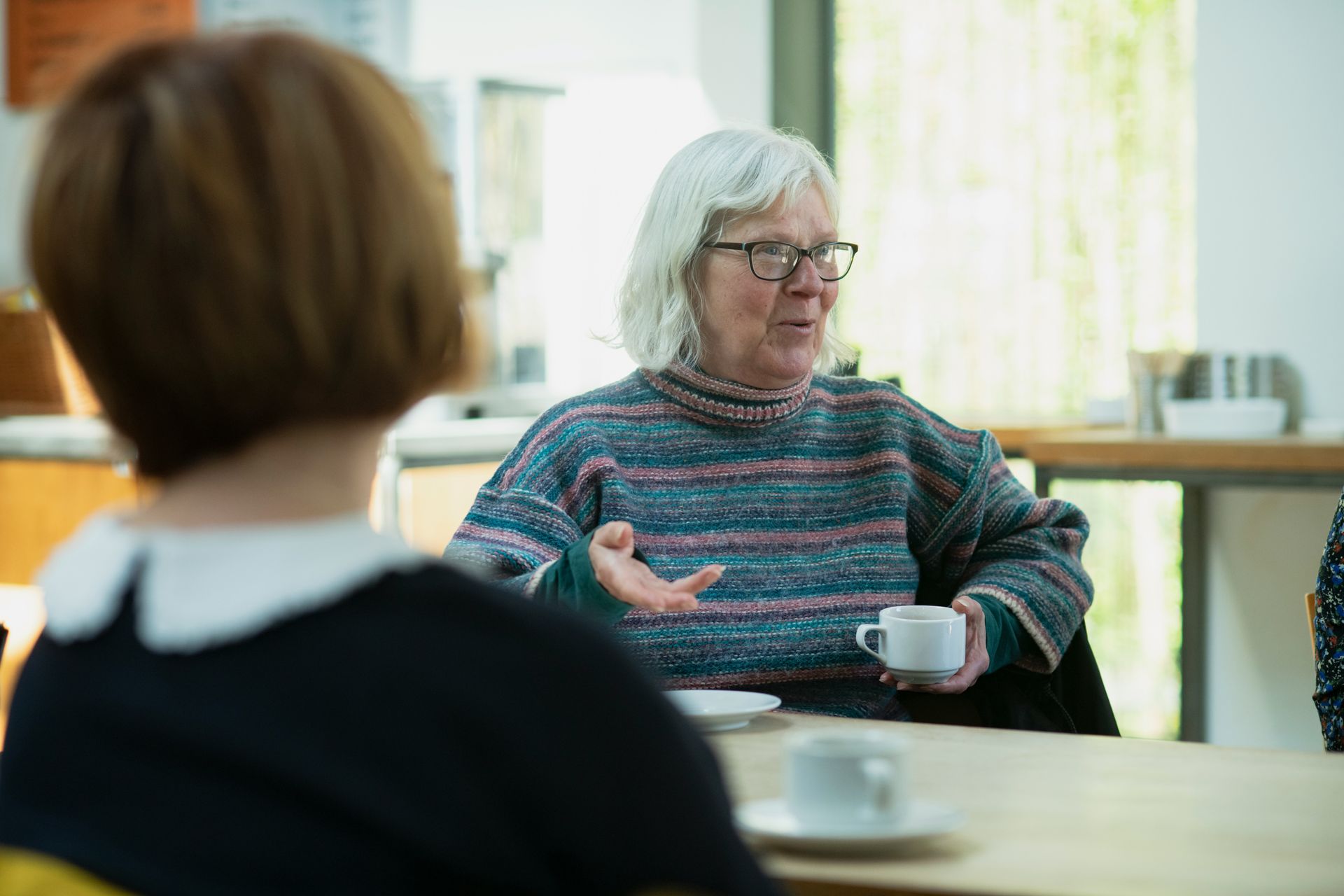 A group of women are drinking tea and chatting at a table indoors .
