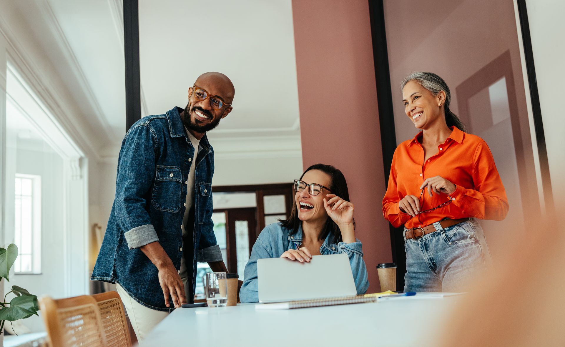Three people are gathered around a laptop looking happy