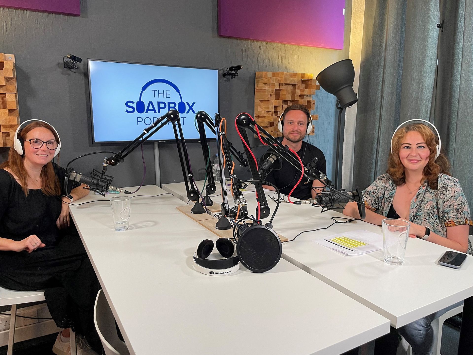 Three people are sitting at a table in front of microphones in a studio.