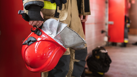 Firefighter holding a red helmet, standing in a fire station.