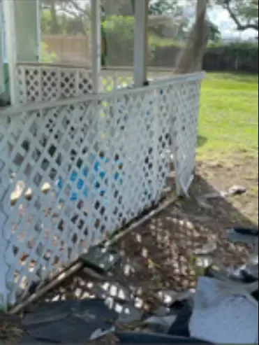 White lattice fence on a porch with debris in front, green grass background.