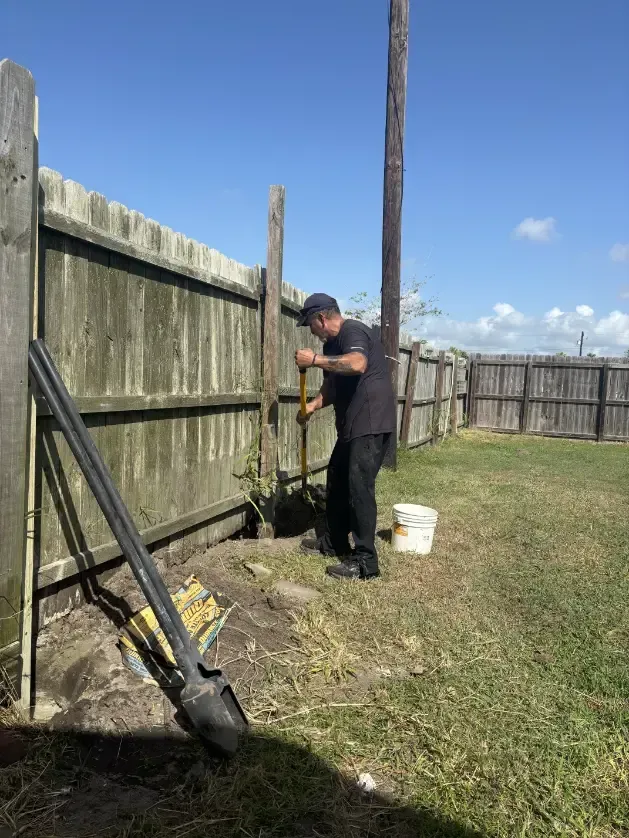 Man digging hole for fence post in backyard.
