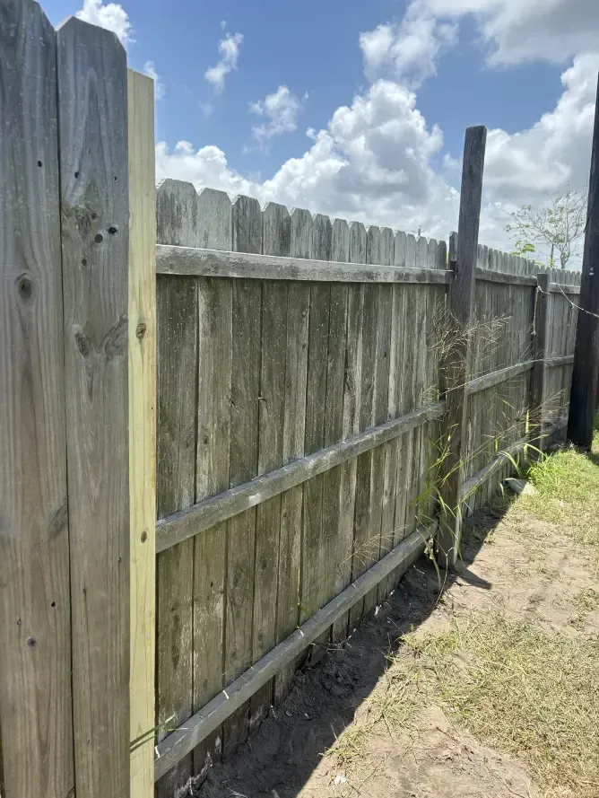 Wooden fence in a yard, with weathered gray planks, a new wooden post, and blue sky.