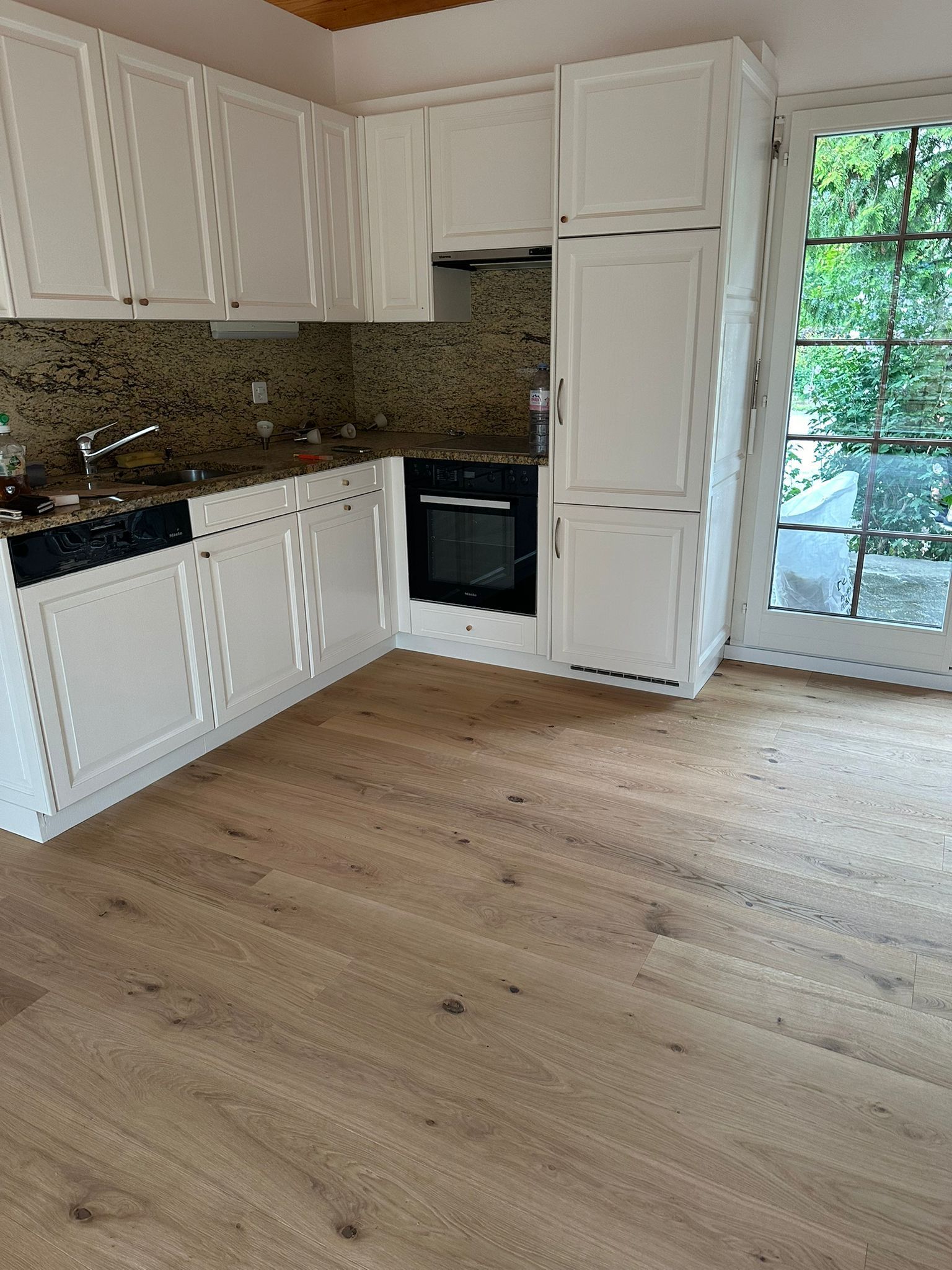 Une cuisine vide avec des armoires blanches et du parquet.