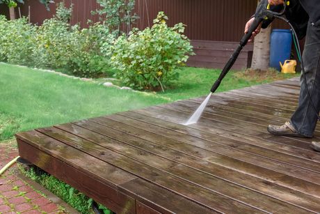 A man is using a high pressure washer to clean a wooden deck.