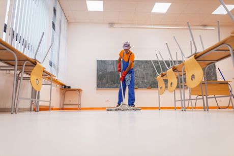 A man is mopping the floor of a classroom.