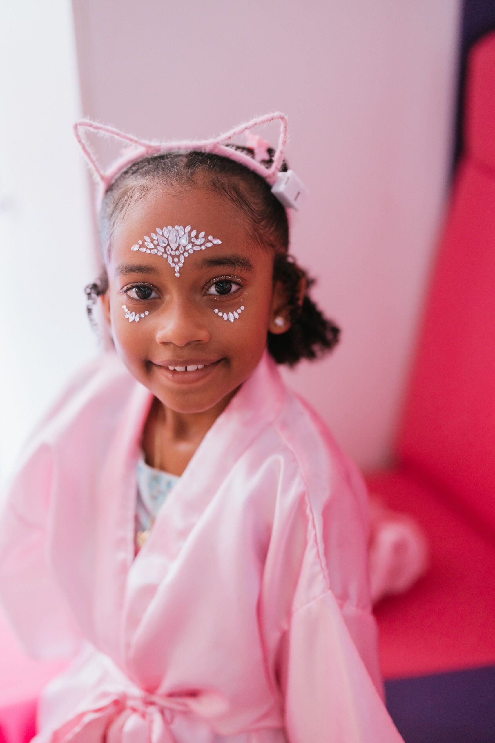 A little girl in a pink robe with cat ears on her head.