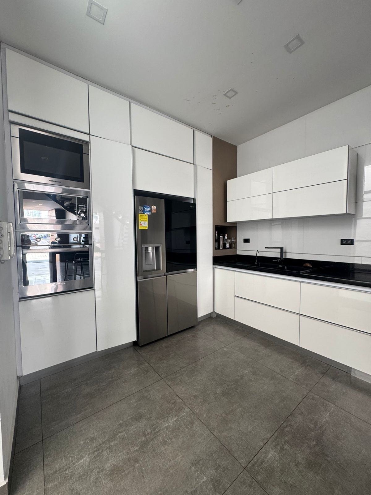 Cocina blanca moderna con electrodomésticos de acero inoxidable, gabinetes y piso de baldosas grises.