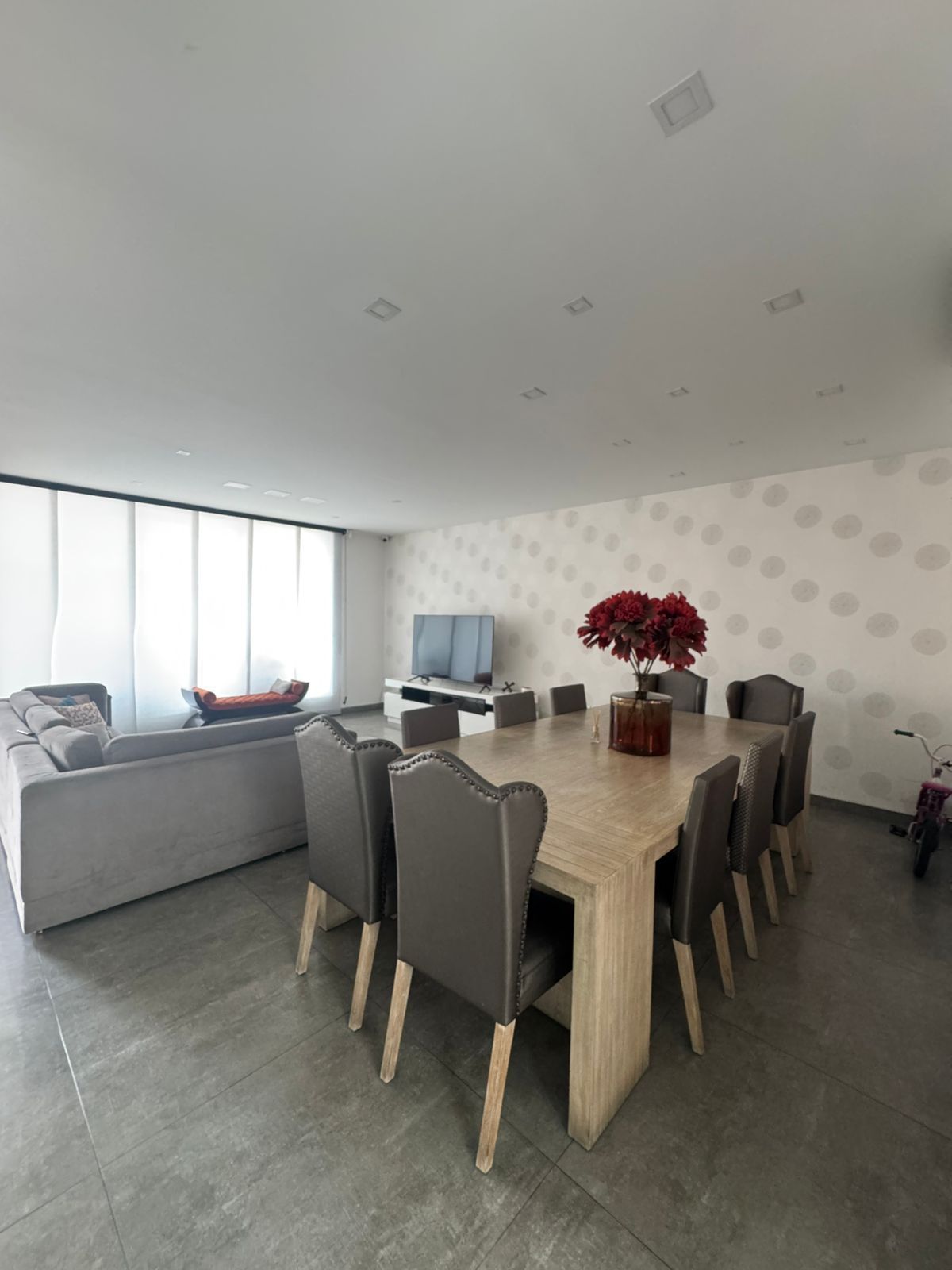 Amplio comedor con gran mesa y sillas, contiguo a una sala de estar con sofá y TV.