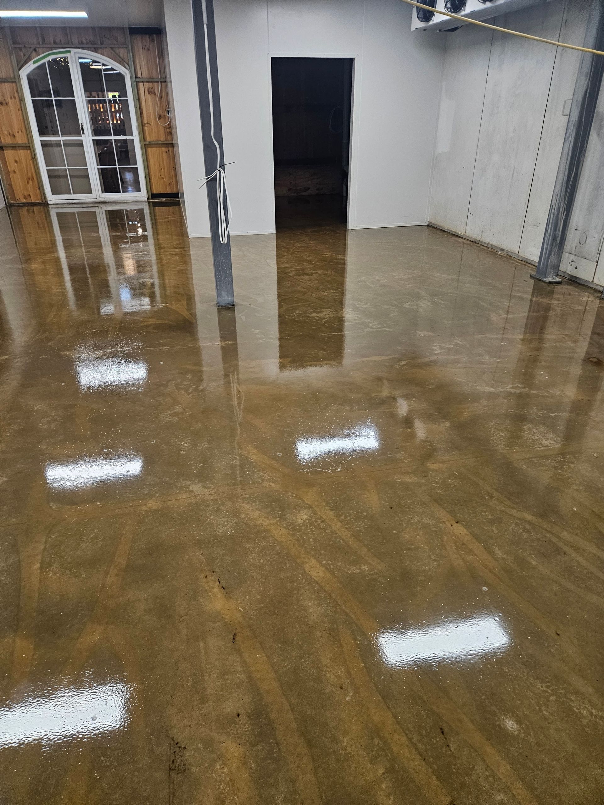 Brown, reflective floor with white patches, interior view. Room has a doorway, arched window, and metal support beams — Riverina Epoxy Flooring In Glenfield Park, NSW