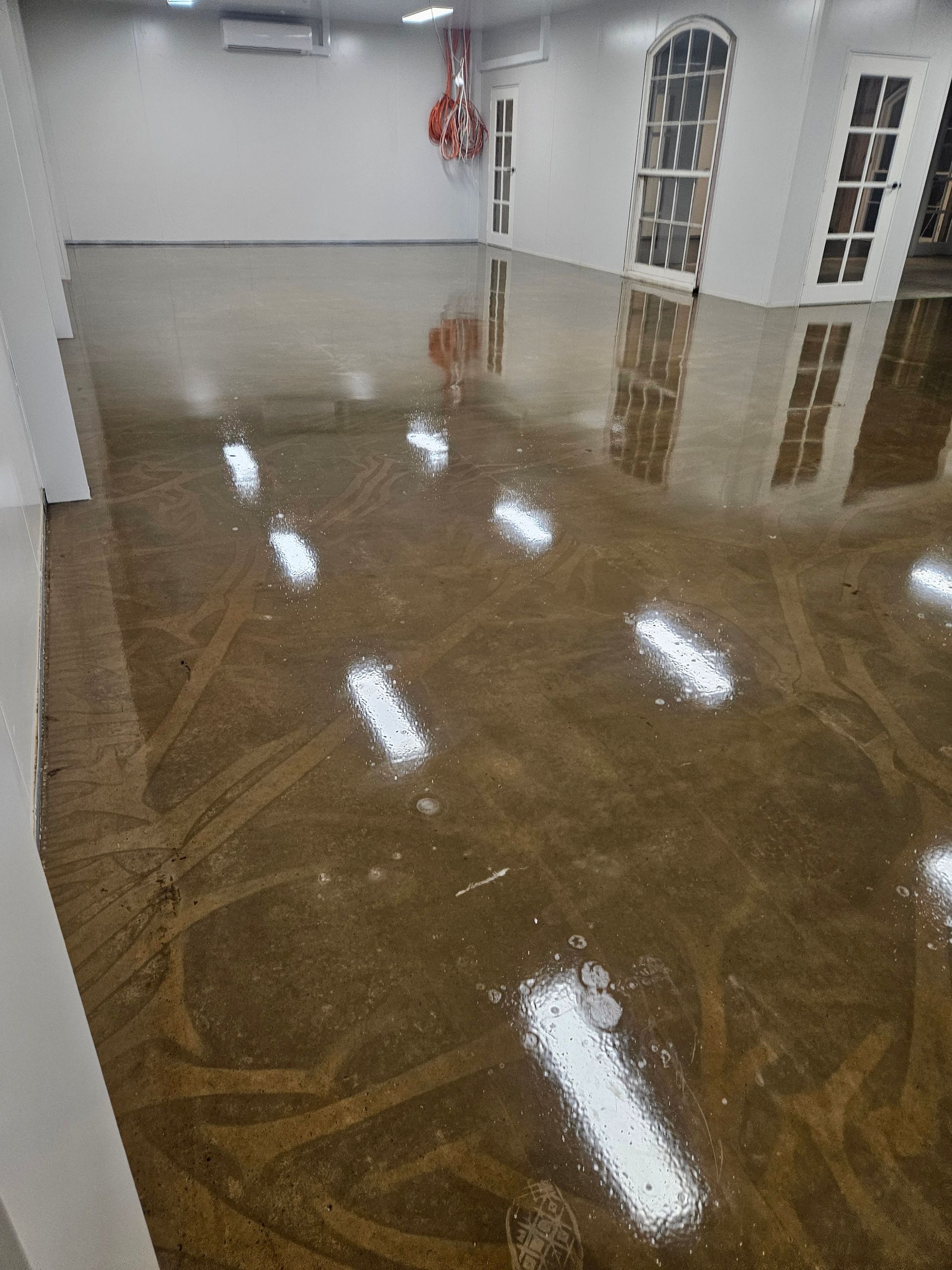Polished brown concrete floor reflects overhead lights in an empty room with white walls and windows — Riverina Epoxy Flooring In Glenfield Park, NSW