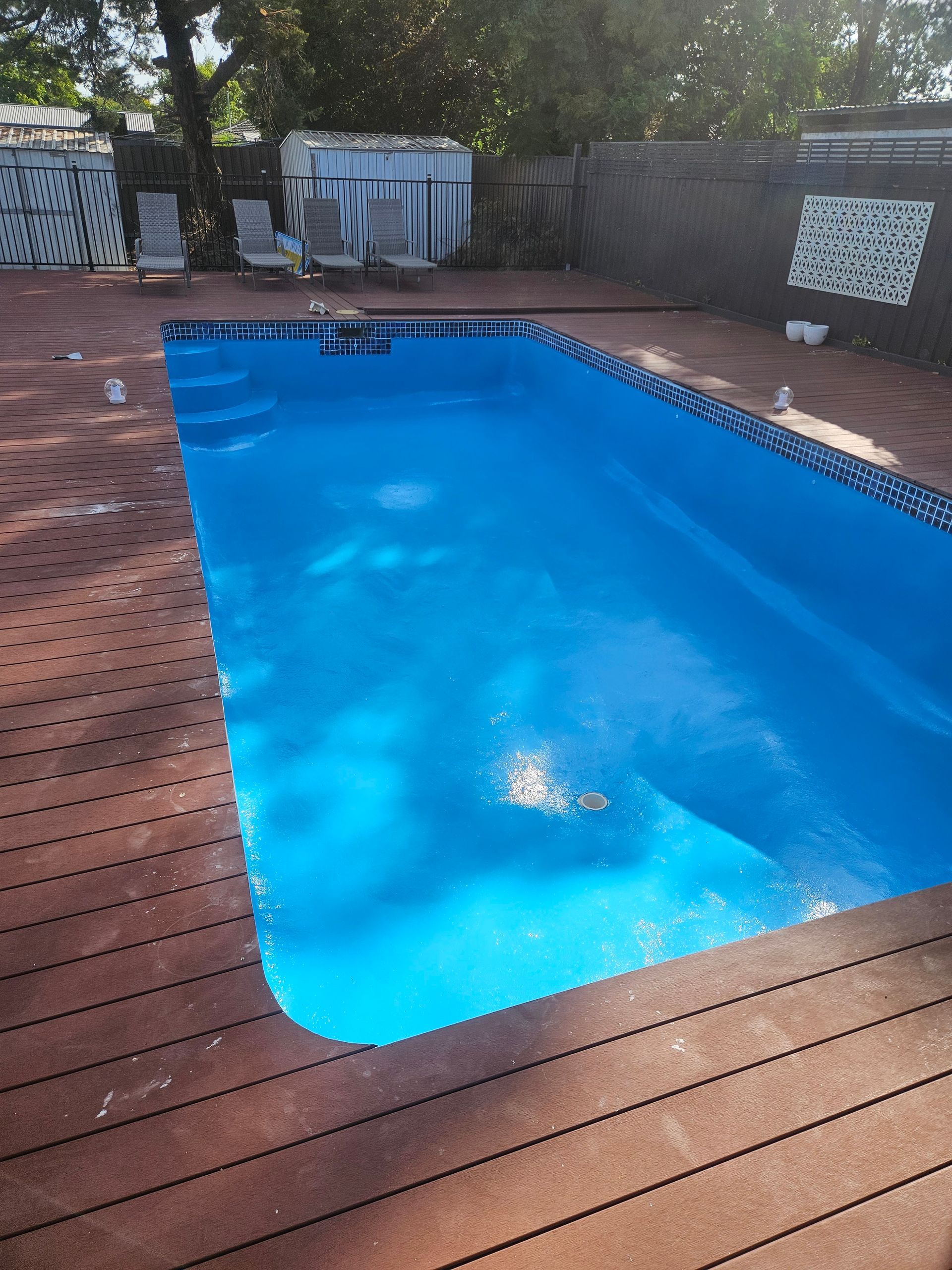 Rectangular blue pool surrounded by a brown wooden deck.  Construction materials in background — Riverina Epoxy Flooring In Glenfield Park, NSW