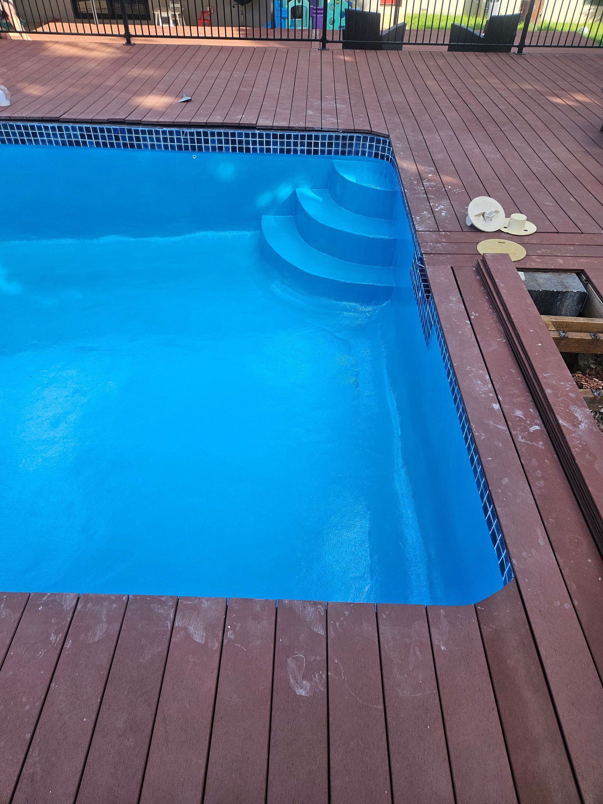 A blue swimming pool with steps, bordered by a brown wooden deck and blue tile — Riverina Epoxy Flooring In Glenfield Park, NSW