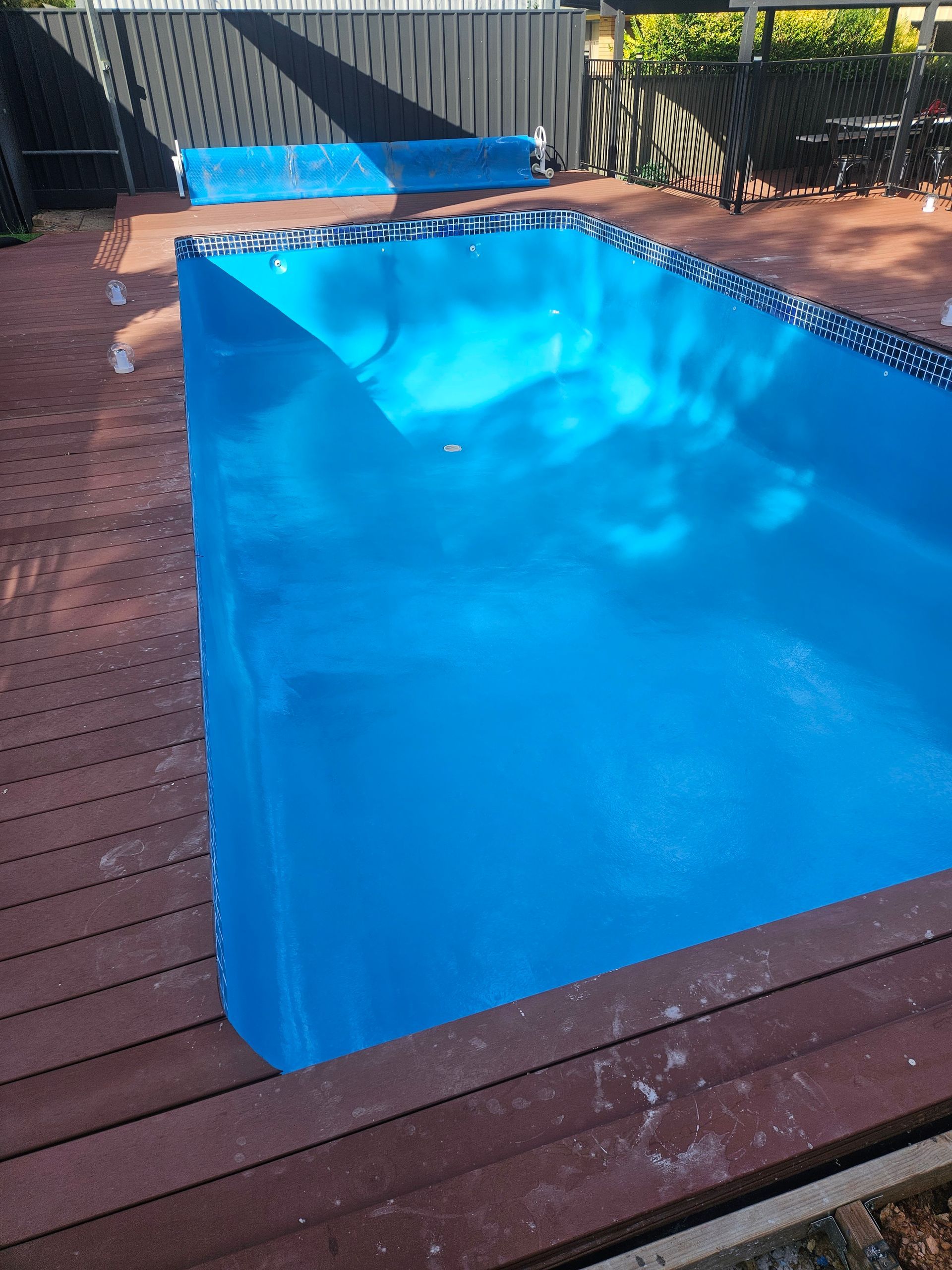 Empty blue swimming pool surrounded by a wooden deck, with a pool cover visible — Riverina Epoxy Flooring In Glenfield Park, NSW