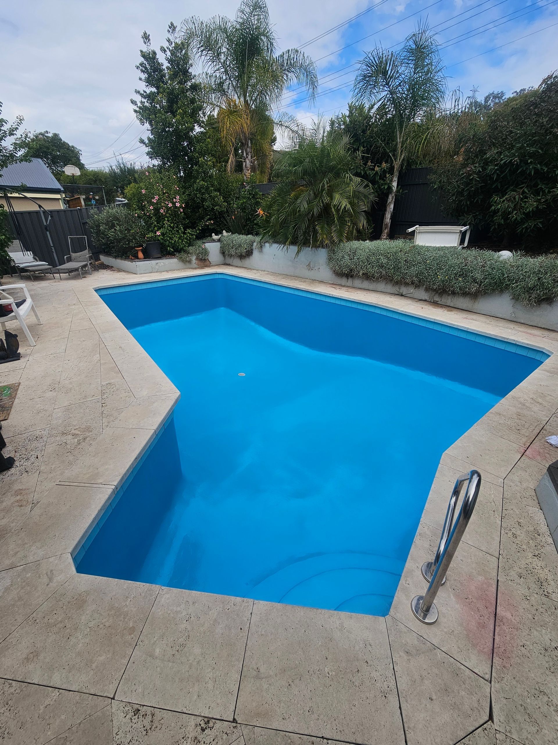 Blue-painted swimming pool surrounded by concrete, with a metal ladder and green shrubbery in the background — Riverina Epoxy Flooring In Glenfield Park, NSW