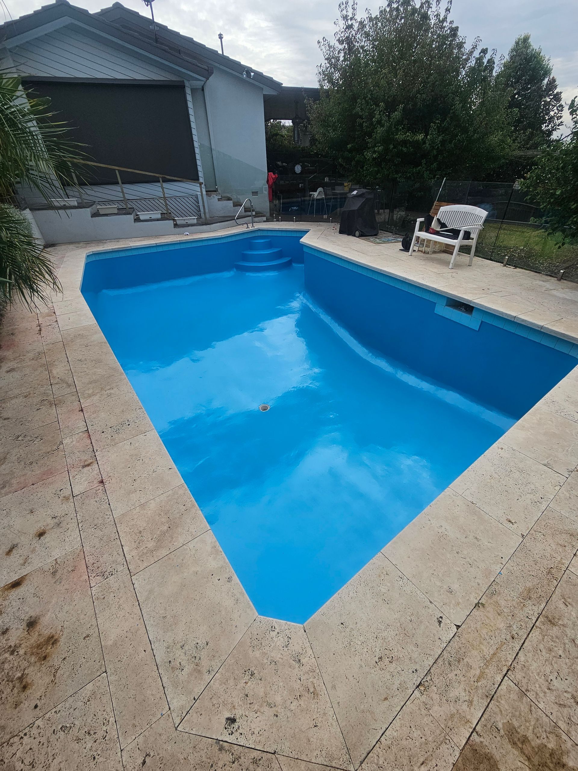 A rectangular swimming pool filled with blue water, set in a stone patio, with a house in the background — Riverina Epoxy Flooring In Glenfield Park, NSW