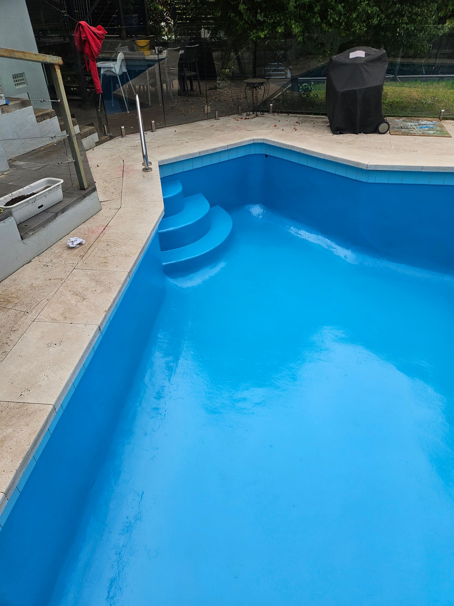 A freshly painted blue swimming pool with steps, concrete border, and a black grill cover — Riverina Epoxy Flooring In Glenfield Park, NSW