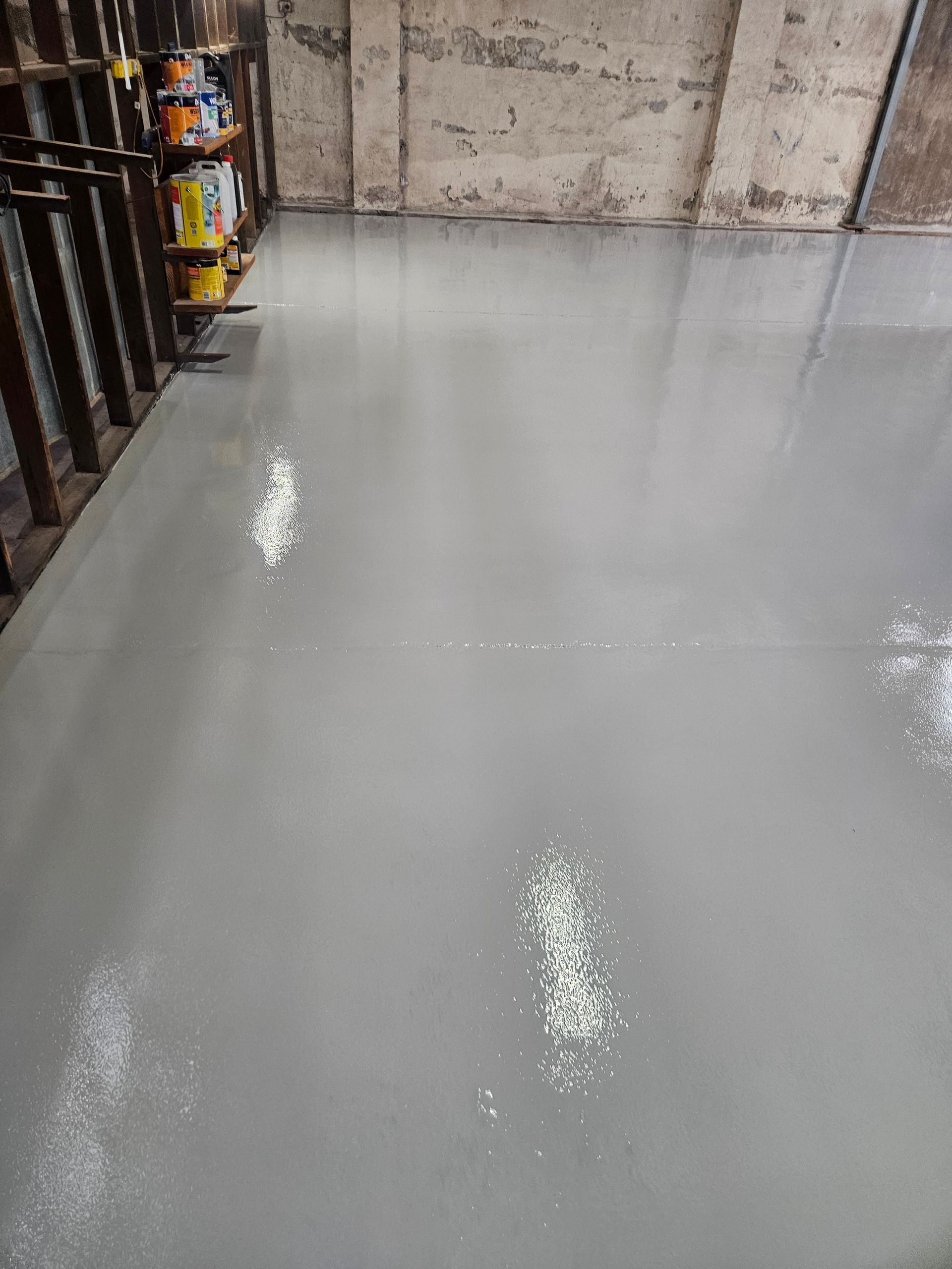 Gray epoxy floor in a warehouse-like setting. Patches of white material are scattered on the floor — Riverina Epoxy Flooring In Glenfield Park, NSW