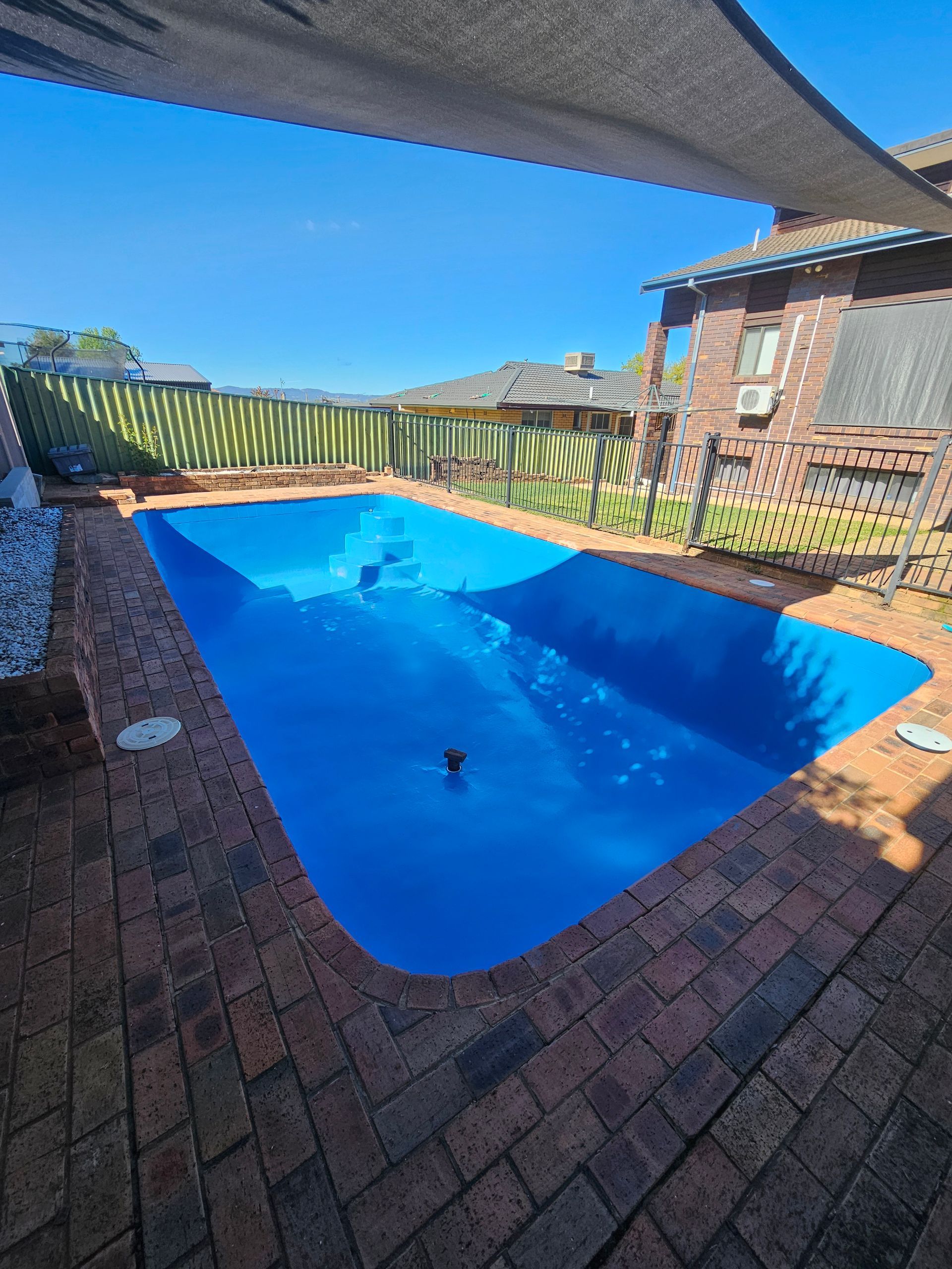Blue-lined rectangular swimming pool in a sunny outdoor setting, surrounded by brick paving and a fence — Riverina Epoxy Flooring In Glenfield Park, NSW