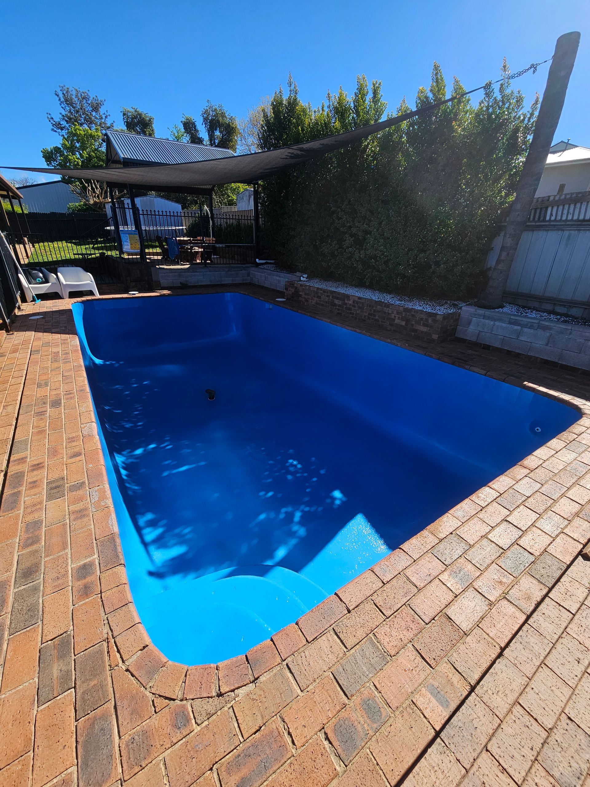 Blue-lined swimming pool surrounded by brick paving and a green hedge — Riverina Epoxy Flooring In Glenfield Park, NSW