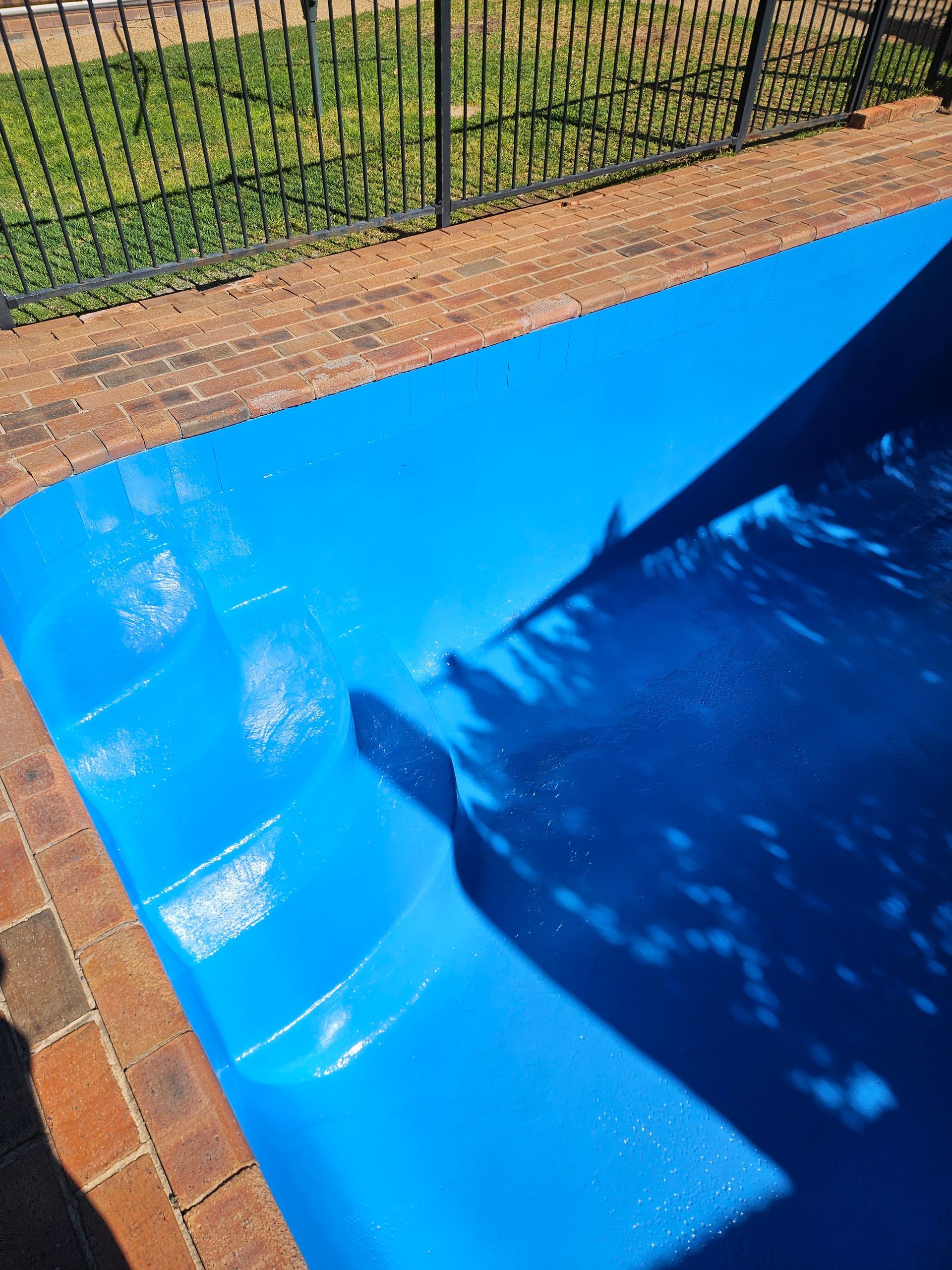 Blue swimming pool with brick edging, a black fence, and tree shadow — Riverina Epoxy Flooring In Glenfield Park, NSW