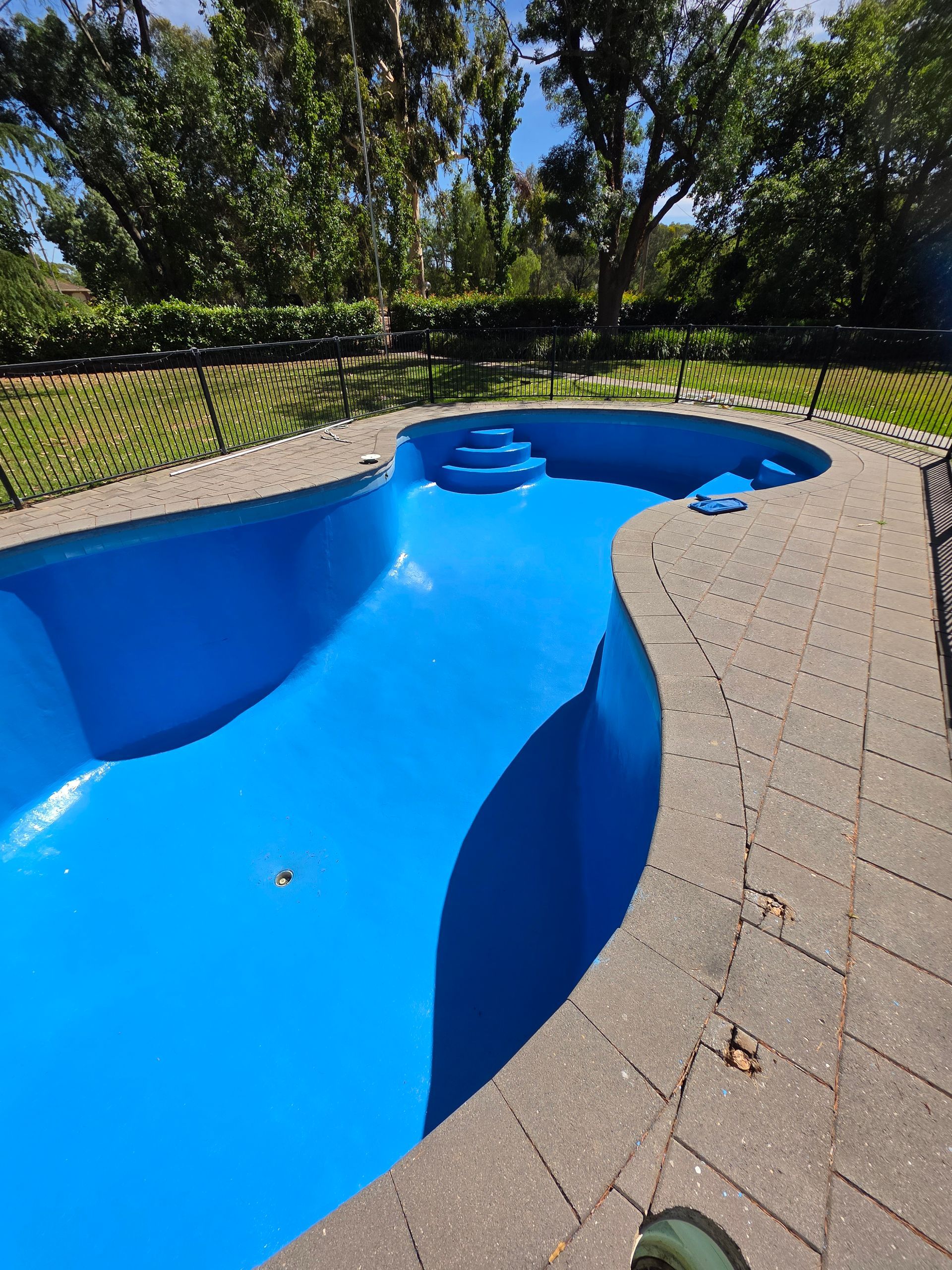 Empty blue swimming pool with steps, surrounded by stone and grass — Riverina Epoxy Flooring In Glenfield Park, NSW
