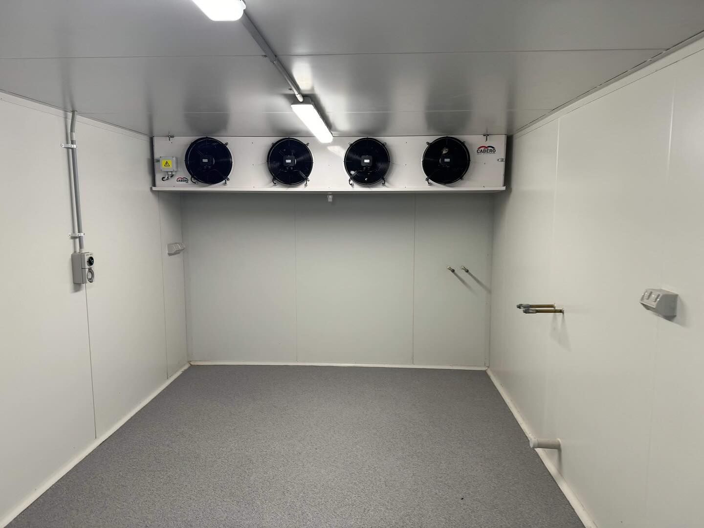 Empty white walk-in freezer with a four-fan unit. Gray floor, fluorescent lights, and electrical components  — Riverina Epoxy Flooring In Glenfield Park, NSW