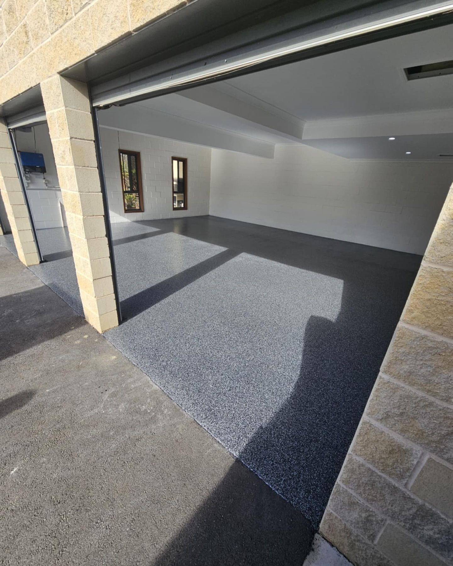 Garage interior with gray speckled flooring, white walls, and open garage door — Riverina Epoxy Flooring In Glenfield Park, NSW