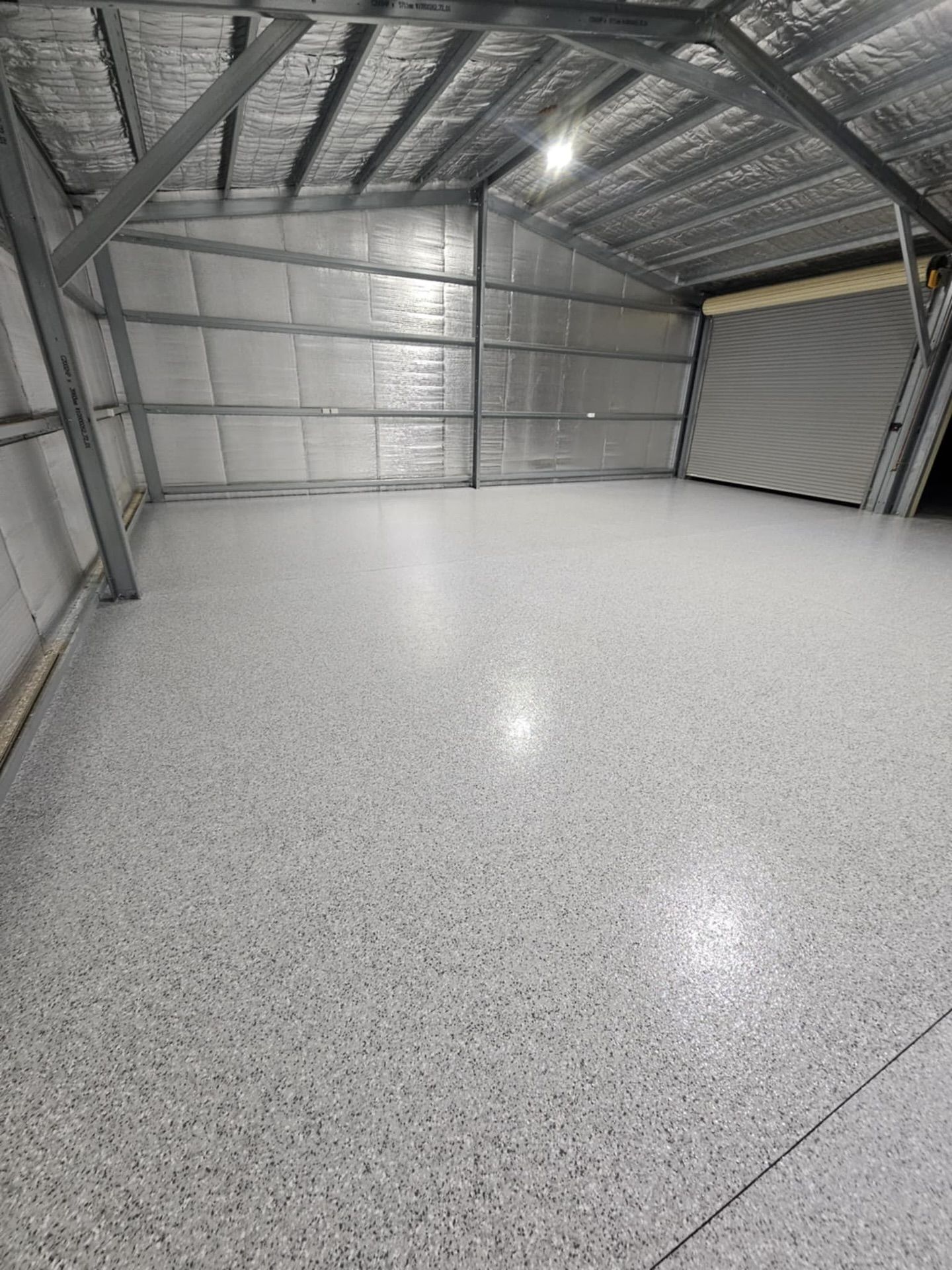 Empty industrial warehouse with gray speckled epoxy flooring and a roll-up door  — Riverina Epoxy Flooring In Glenfield Park, NSW