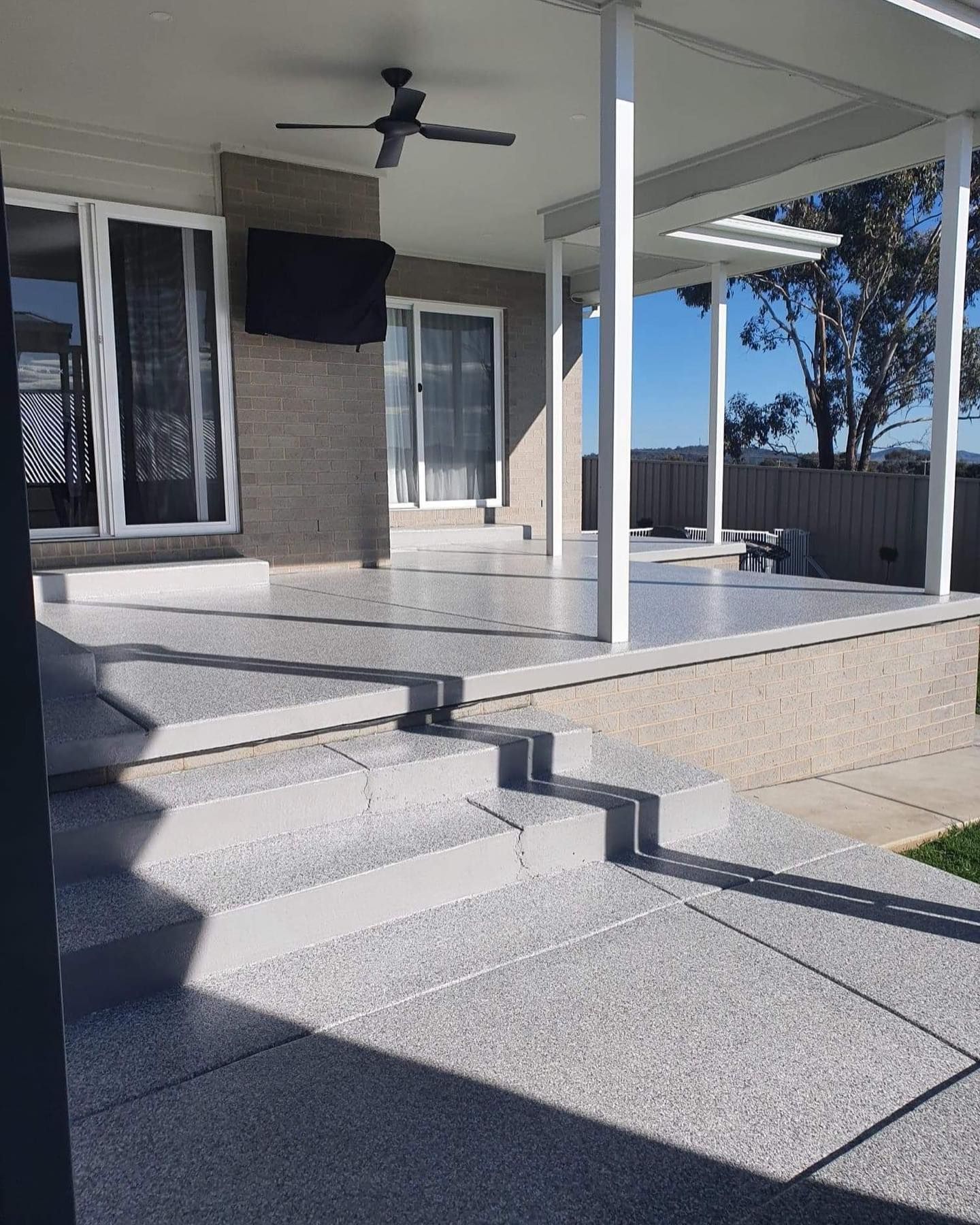 Gray concrete patio with steps leading to a covered area with white posts and ceiling fan — Riverina Epoxy Flooring In Glenfield Park, NSW