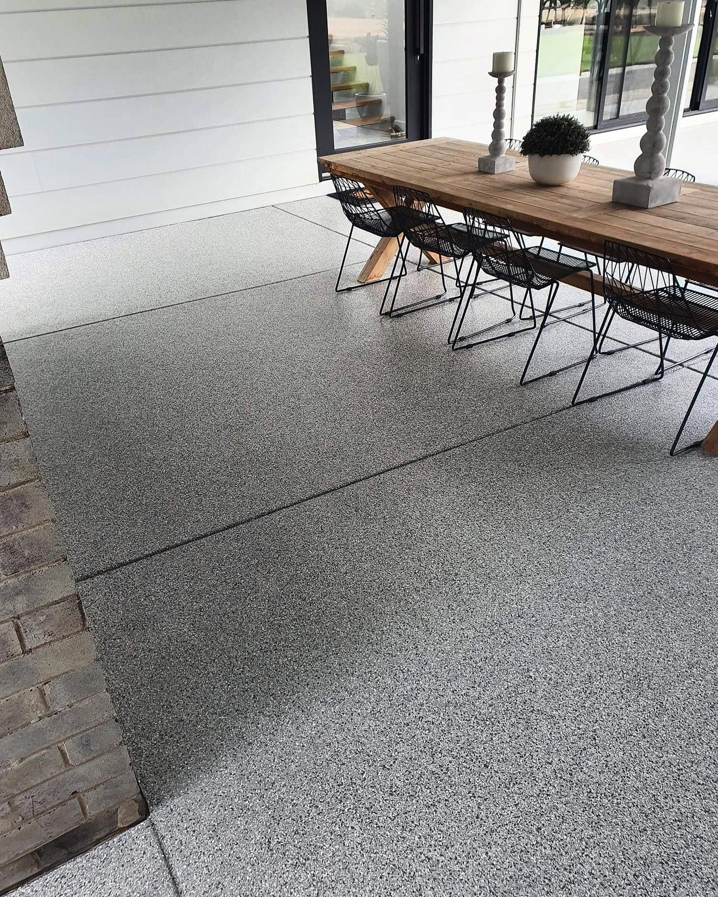 Outdoor patio with speckled gray flooring, a wooden table, and black wire chairs — Riverina Epoxy Flooring In Glenfield Park, NSW