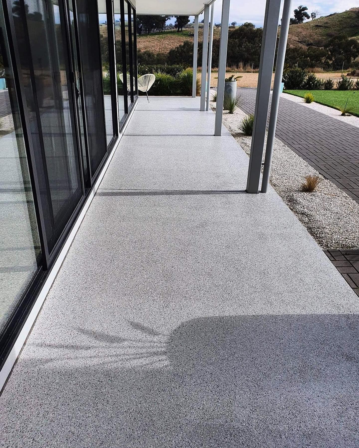 Gray speckled concrete walkway next to a building with large windows and a covered patio area — Riverina Epoxy Flooring In Glenfield Park, NSW