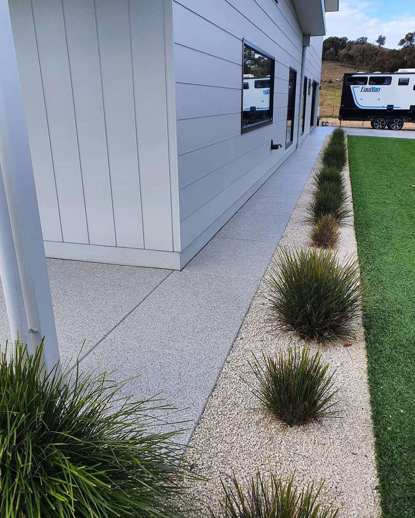 Exterior view of a modern building with a concrete walkway, small bushes, and a green lawn — Riverina Epoxy Flooring In Glenfield Park, NSW
