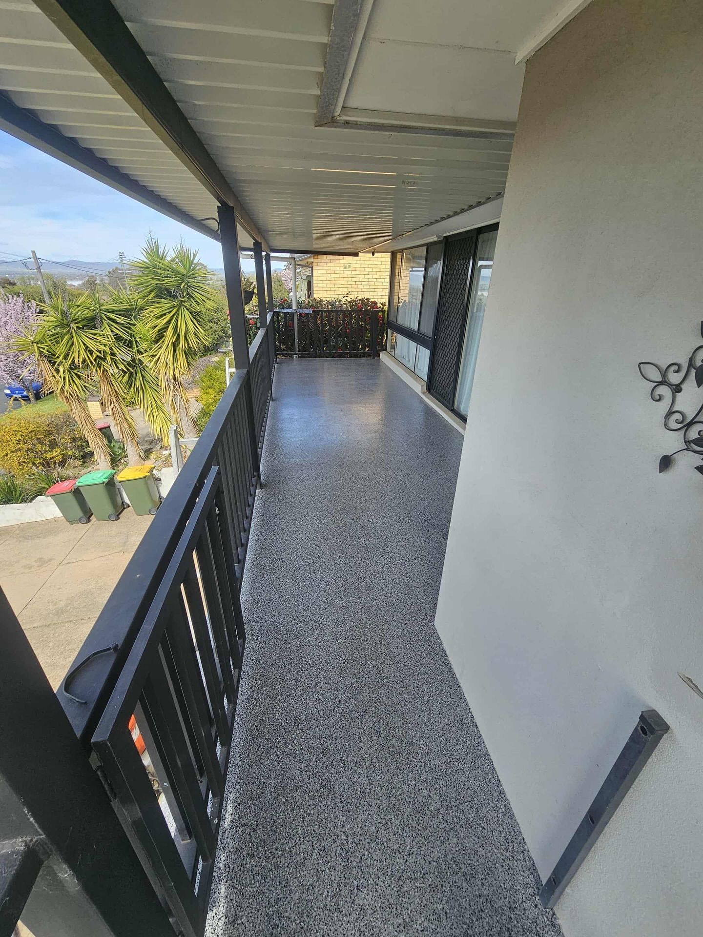 Balcony with black railing, speckled floor, and view of trees and houses — Riverina Epoxy Flooring In Glenfield Park, NSW