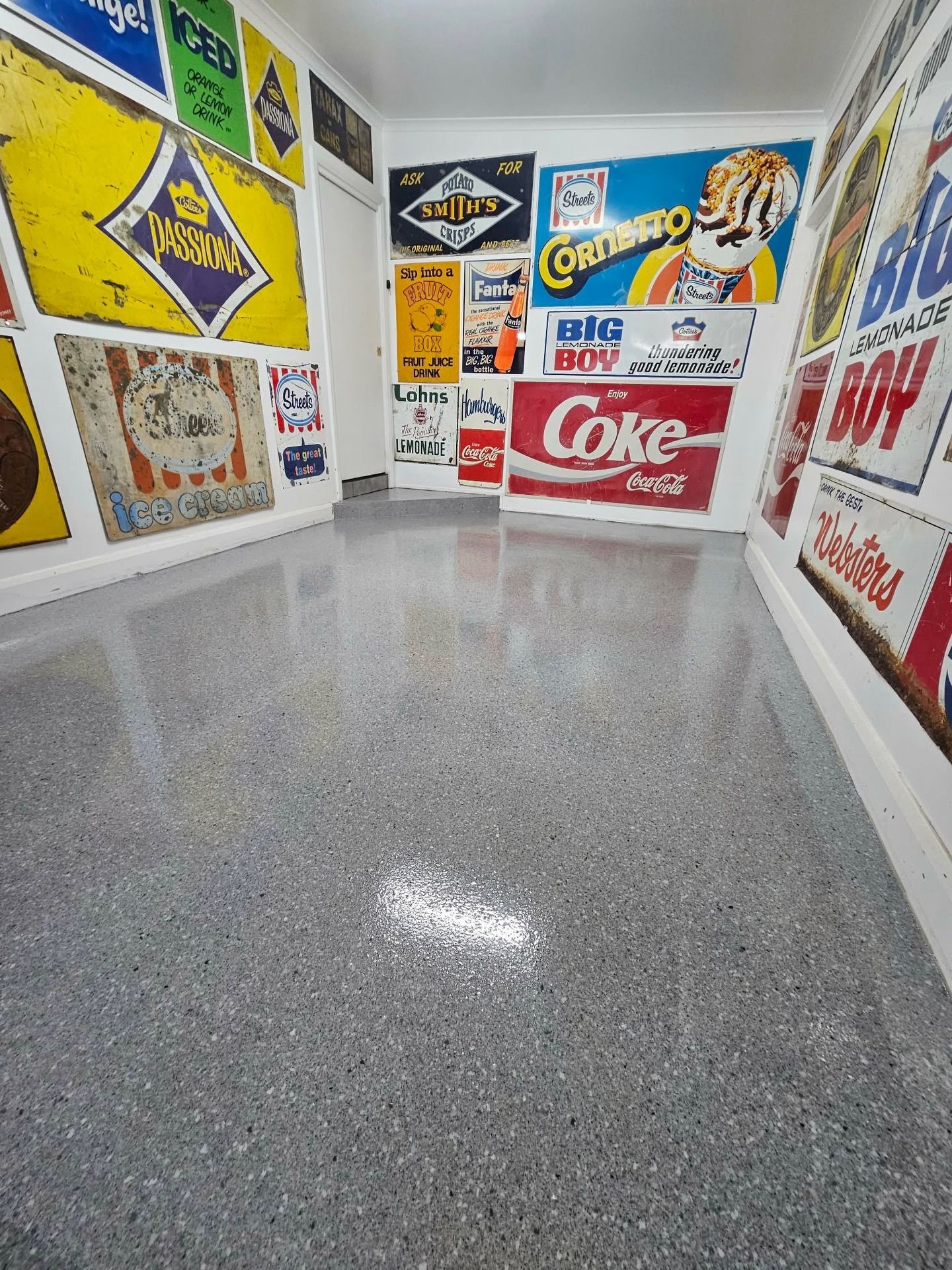 Narrow hallway with gray speckled floor, walls lined with vintage advertising signs — Riverina Epoxy Flooring In Glenfield Park, NSW