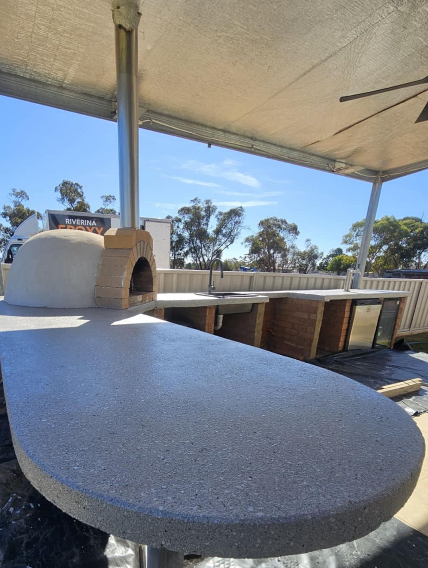 Outdoor kitchen with pizza oven, concrete countertop, under a covered patio on a sunny day — Riverina Epoxy Flooring In Glenfield Park, NSW