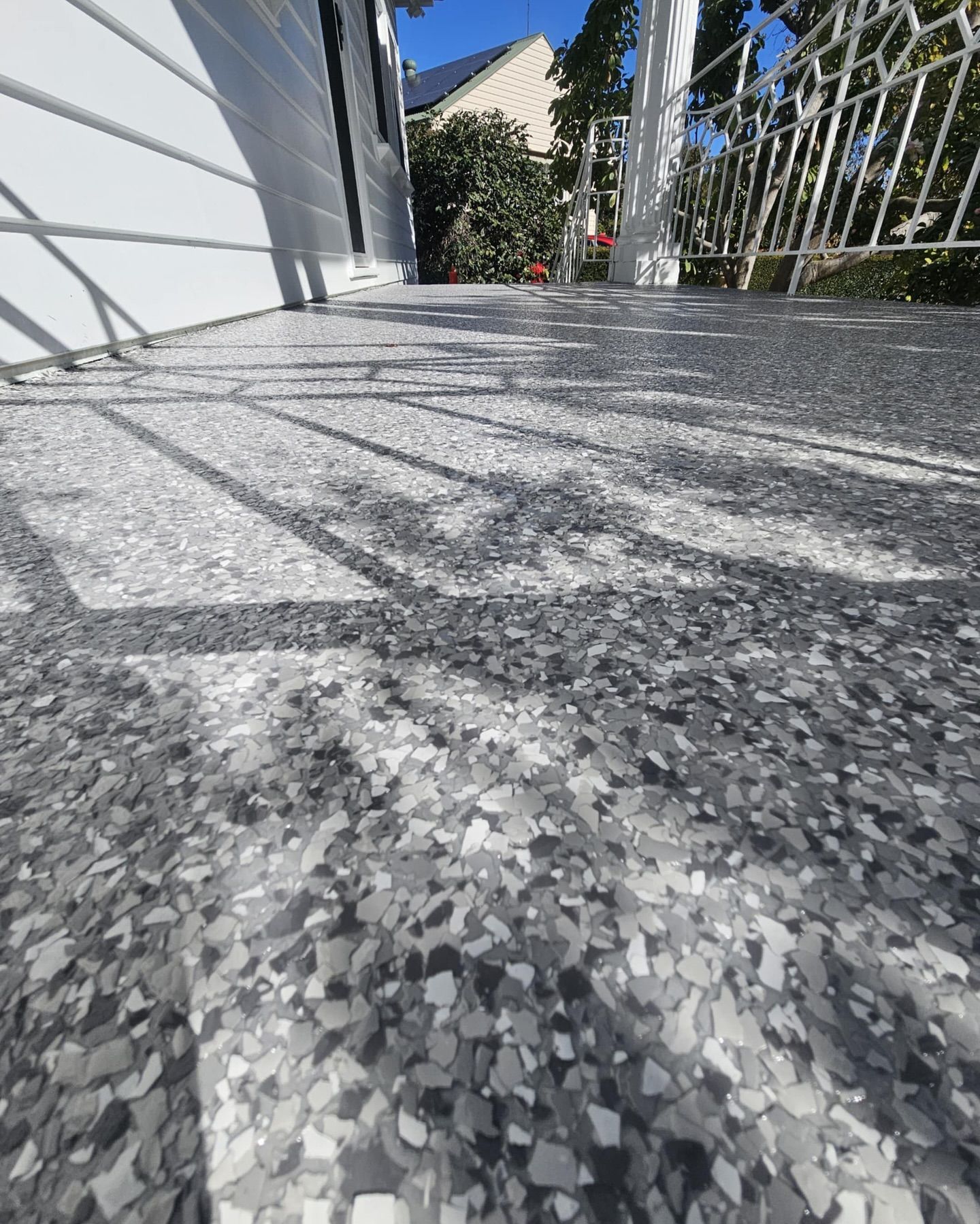 Gray speckled concrete surface with a white railing and wall in the background. Sunlight casts shadows — Riverina Epoxy Flooring In Glenfield Park, NSW
