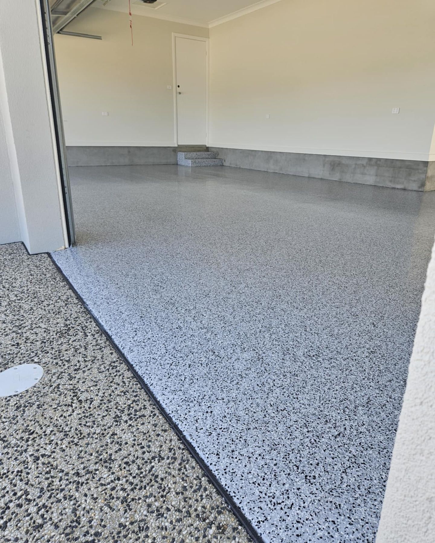 Garage with a speckled epoxy floor; off-white walls. Door and garage door visible — Riverina Epoxy Flooring In Glenfield Park, NSW