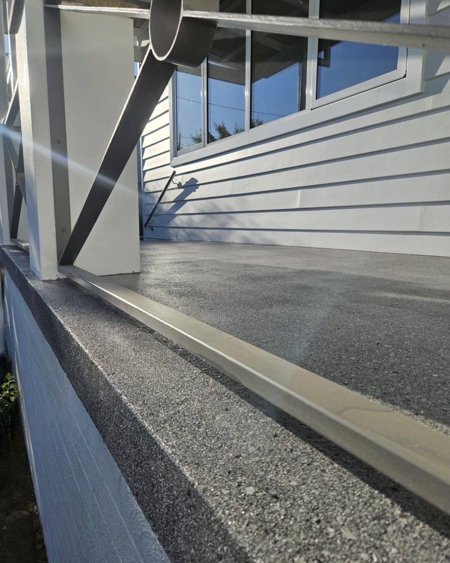 Gray concrete deck with metal railing and support beam. White siding in the background — Riverina Epoxy Flooring In Glenfield Park, NSW