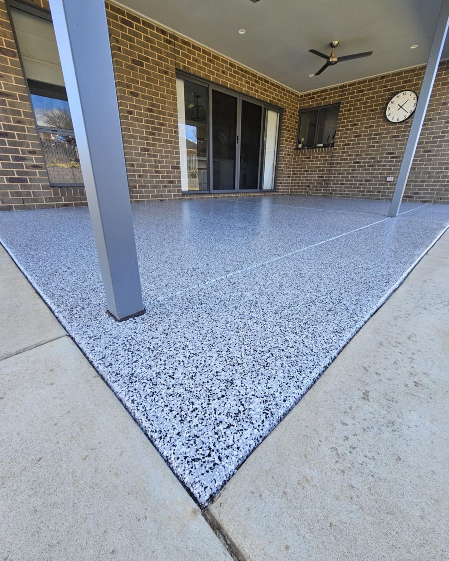 Patio with speckled, gray concrete floor, brick wall, sliding glass door, and metal support beams — Riverina Epoxy Flooring In Glenfield Park, NSW