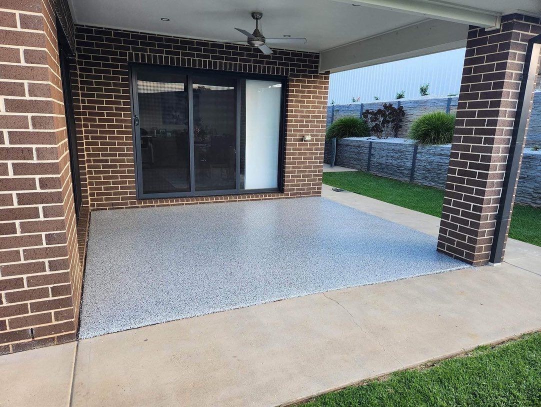 Patio with speckled concrete floor, brick walls, sliding glass door, and green grass — Riverina Epoxy Flooring In Glenfield Park, NSW