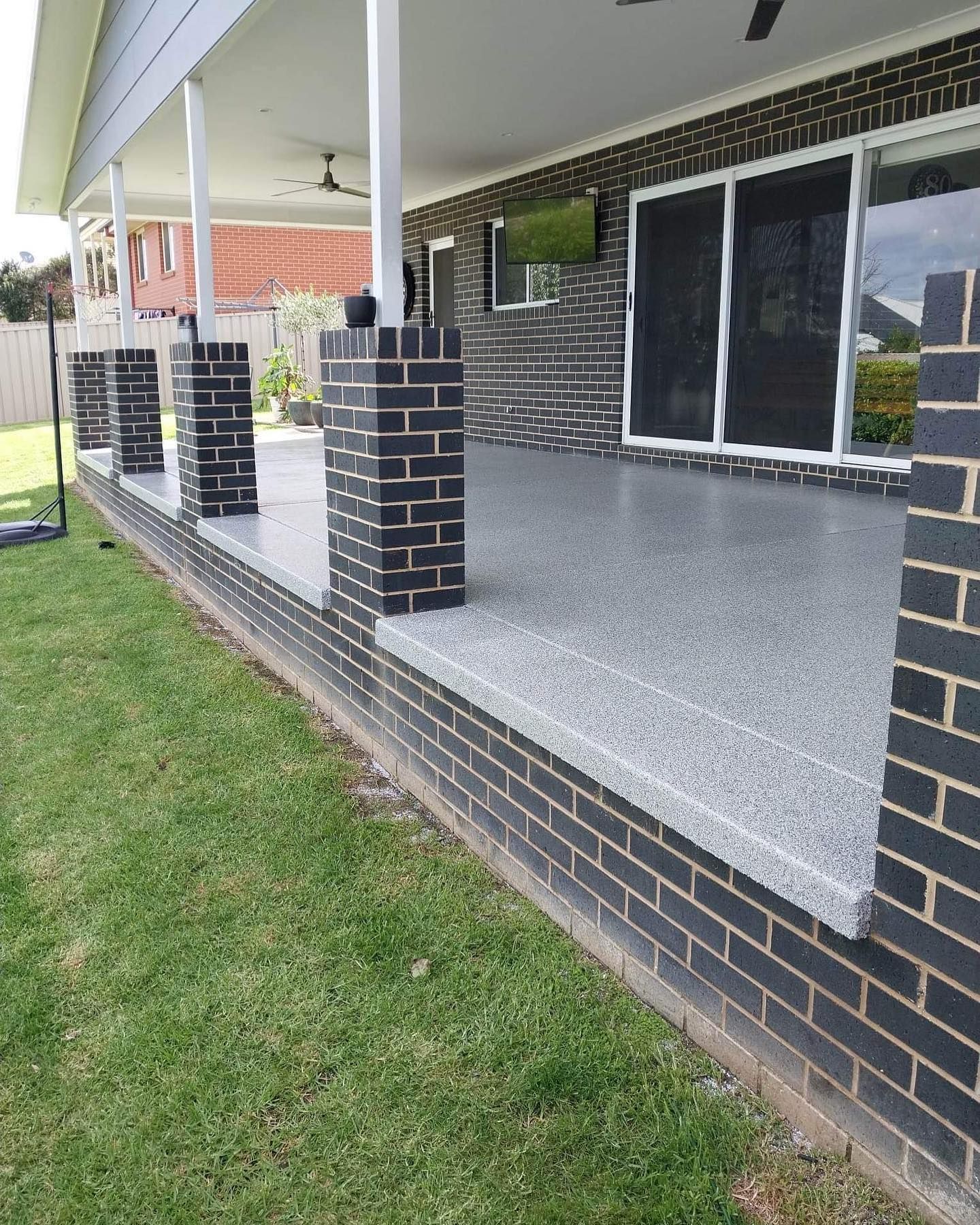 A covered porch with gray flooring, brick pillars, and a brick wall. Green grass is in the foreground — Riverina Epoxy Flooring In Glenfield Park, NSW