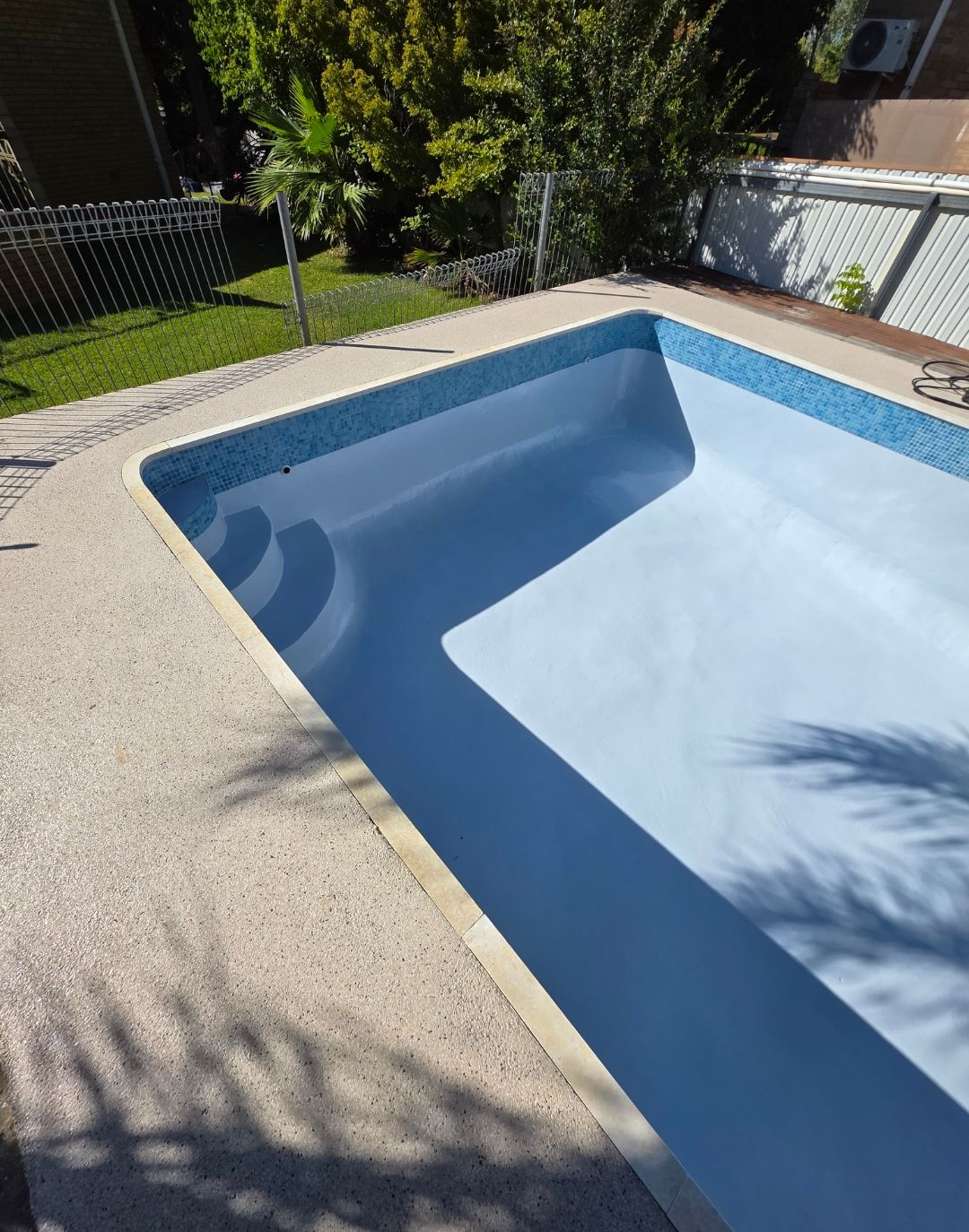 Empty rectangular pool with light blue interior, blue tile border, surrounded by concrete — Riverina Epoxy Flooring In Glenfield Park, NSW
