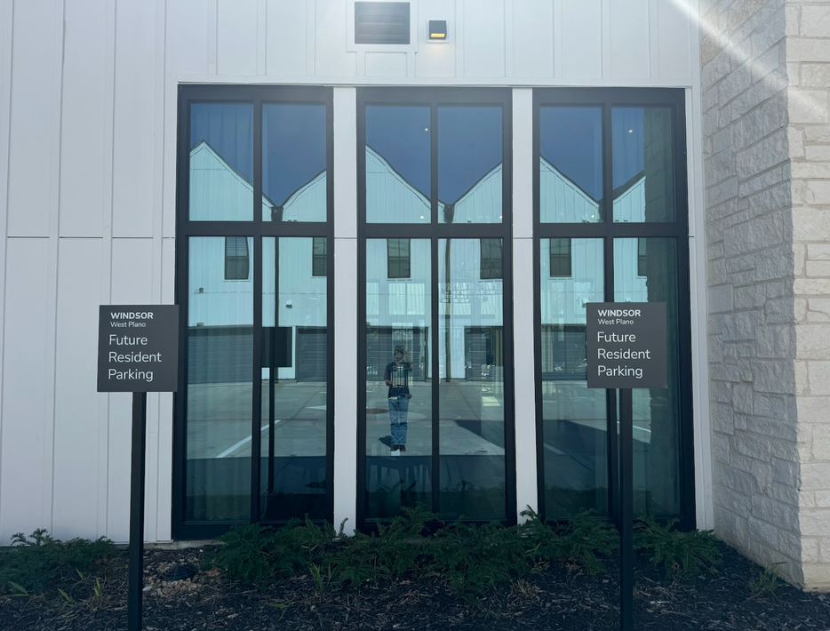 Glass double doors with dark frames on a white building entrance, flanked by small black signs.