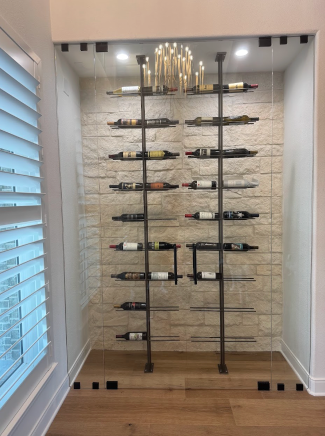 Small closet with wall-mounted glass shelves and a gold chandelier, lit by recessed ceiling lights.