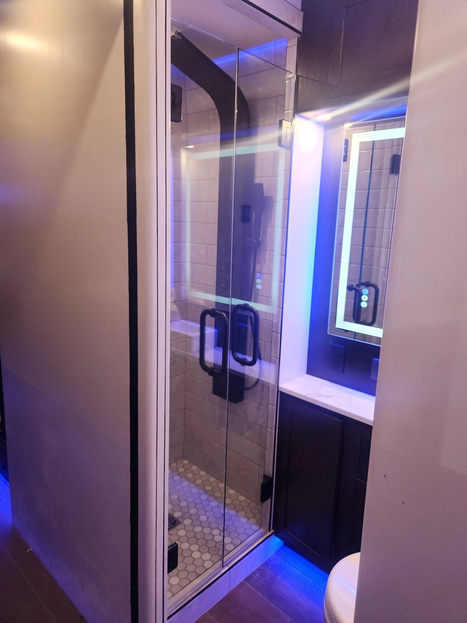Small bathroom with glass shower door, lit vanity mirror, and blue accent lighting.