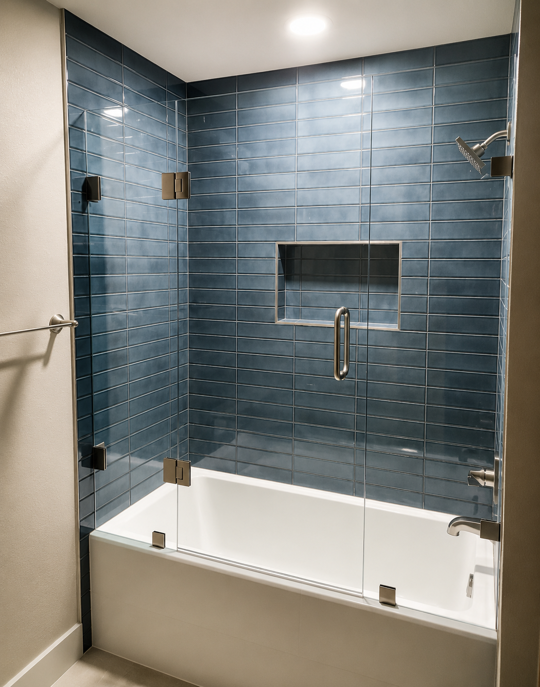 Blue-tiled glass shower enclosure with white tub and brass fixtures in a bathroom