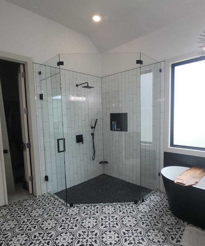 Modern bathroom with glass shower, black-and-white tile floor, and window nook with wood seat